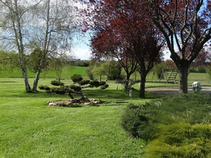 A well-maintained park with various trees, a grassy area, and a wooden swing set.