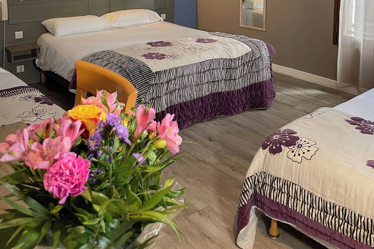 Une chambre d’hôtel avec deux lits, un plancher en bois, un miroir et un vase de fleurs.