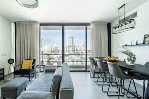Una sala de estar moderna con un ventanal grande, un sofá, una mesa de comedor y vistas a la ciudad.