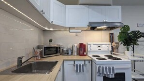 A modern kitchen with white cabinets, a stainless steel sink, a microwave, a toaster, a coffee maker, and a stove. - Stylish Studio, Steps to Transit (Montréal)