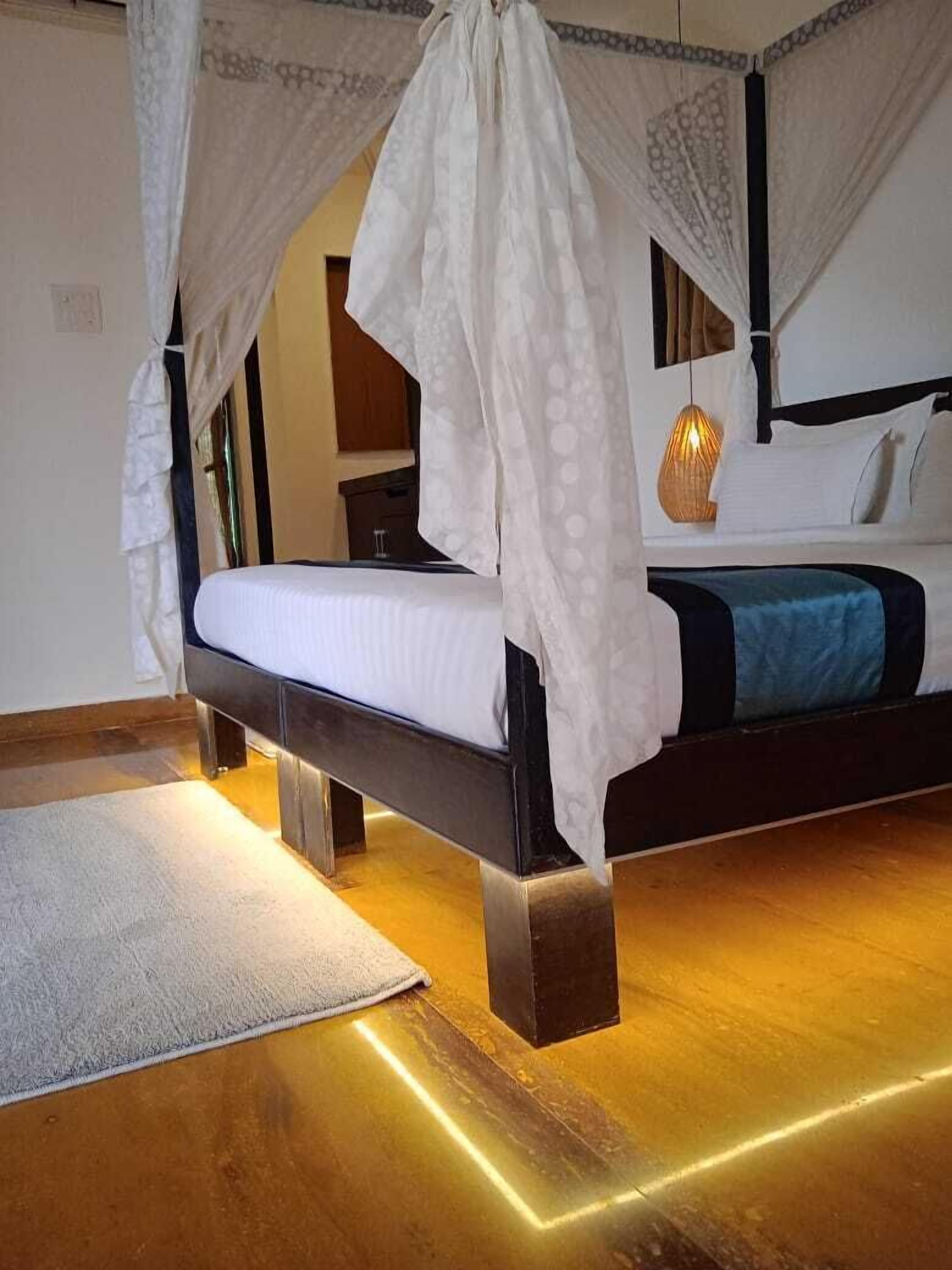 A bedroom with a four-poster canopy bed, a bedside table, and a nightstand.