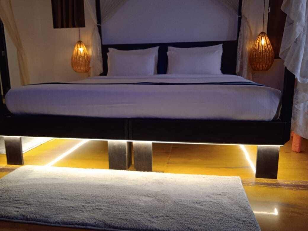 A bed with a headboard, two bedside lamps, and a bedside table with a lamp.