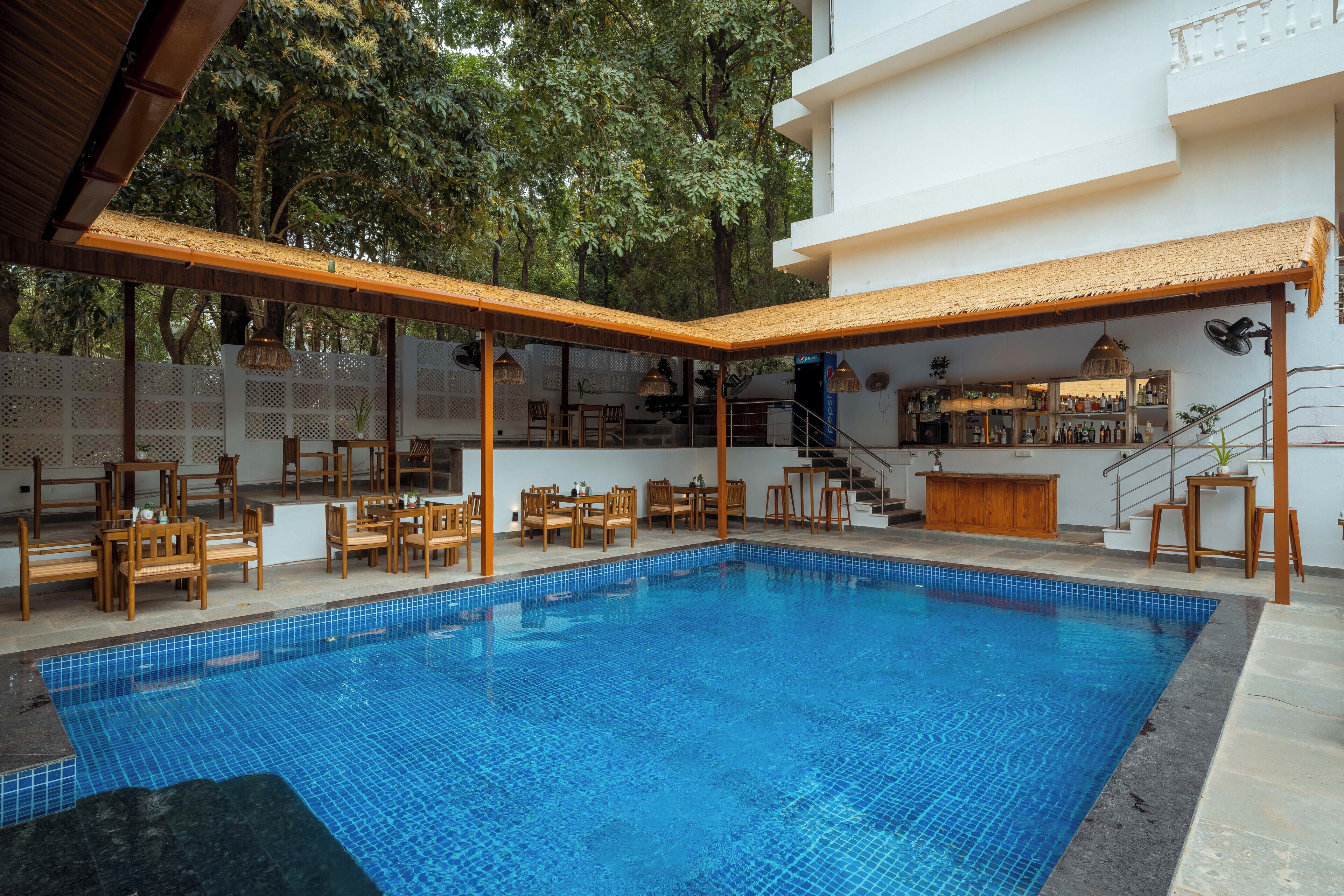 A swimming pool with tiled blue floor, wooden chairs, and a bar area with shelves of bottles.