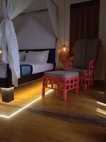 Un dormitorio con cama, una silla, una mesita y una lámpara de noche.