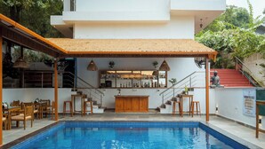 A modern pool area with a bar, seating, and a staircase leading to a second floor. - Verandah Goa (Anjuna)