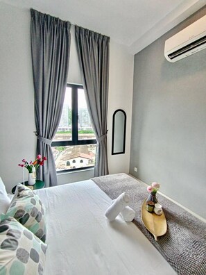 A hotel room with a bed, a small table with a vase of flowers, and a view of buildings outside the window. - The Horizon Ipoh 2BR L11 by Grab A Stay (Ipoh)