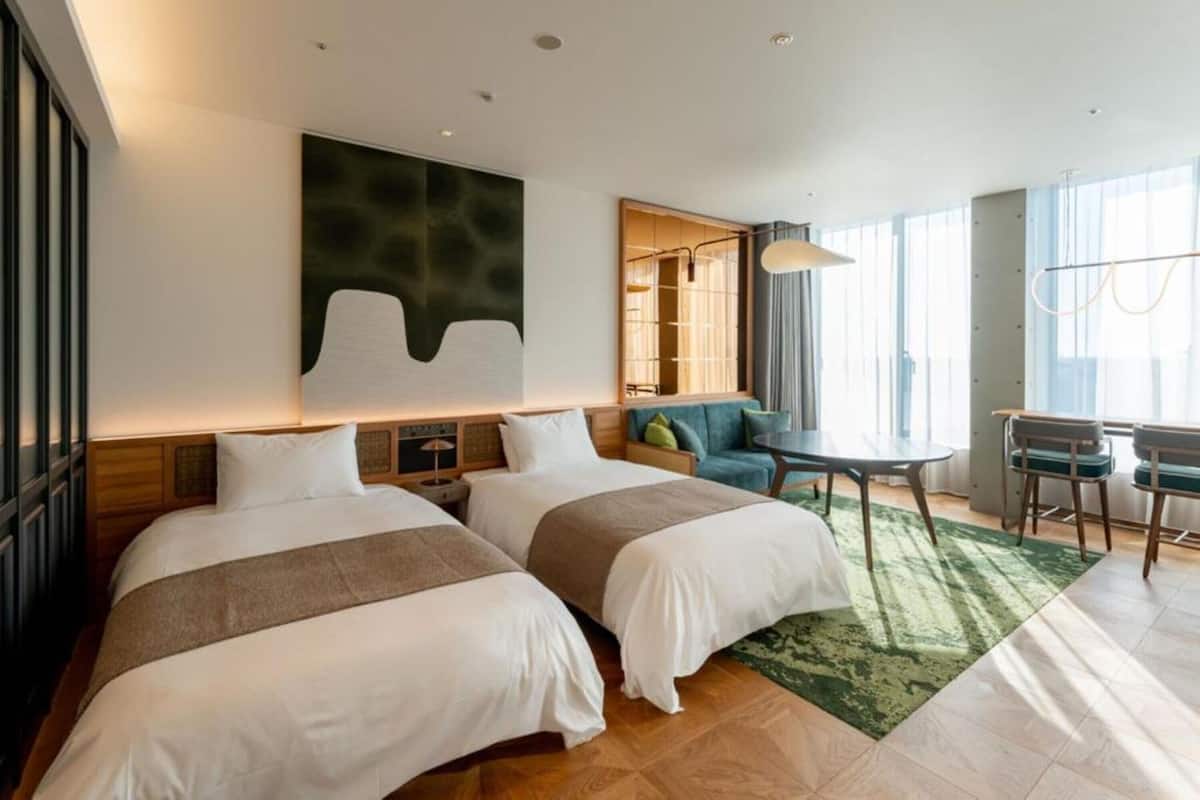 A hotel room with two beds, a dining area, and a large window.