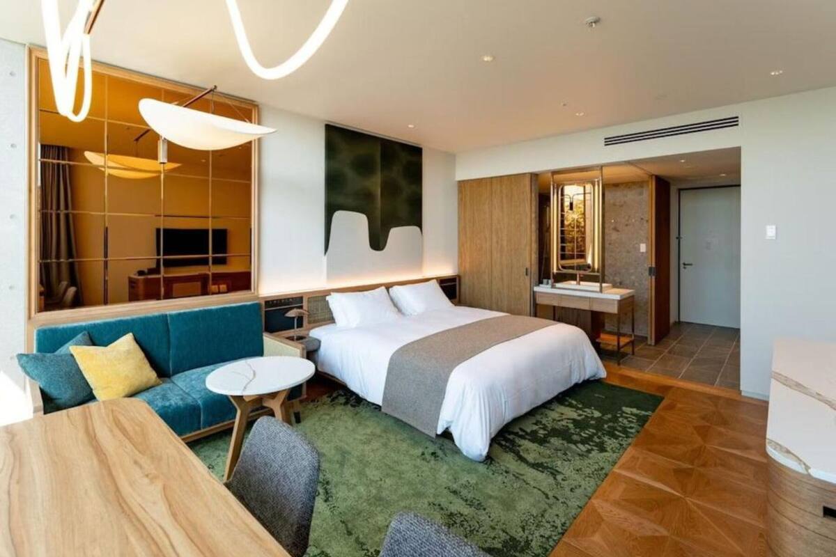 A modern hotel room with a bed, a sofa, a small table, and a desk.