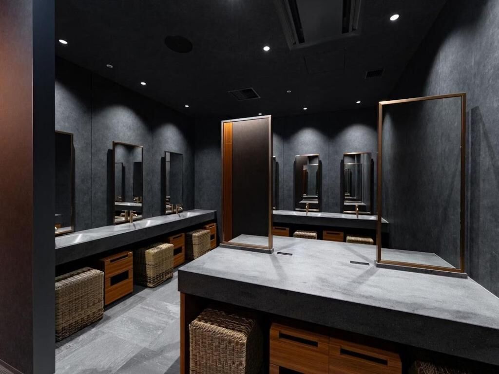 Une salle de bain moderne avec des murs sombres, de grands miroirs et des boîtes de rangement en bois.