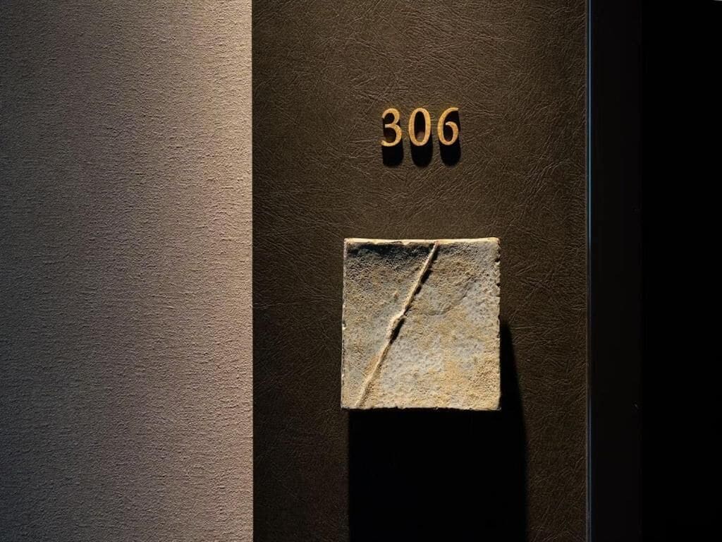 Paret fosca i amb textura, amb el número '306' i una placa de pedra.