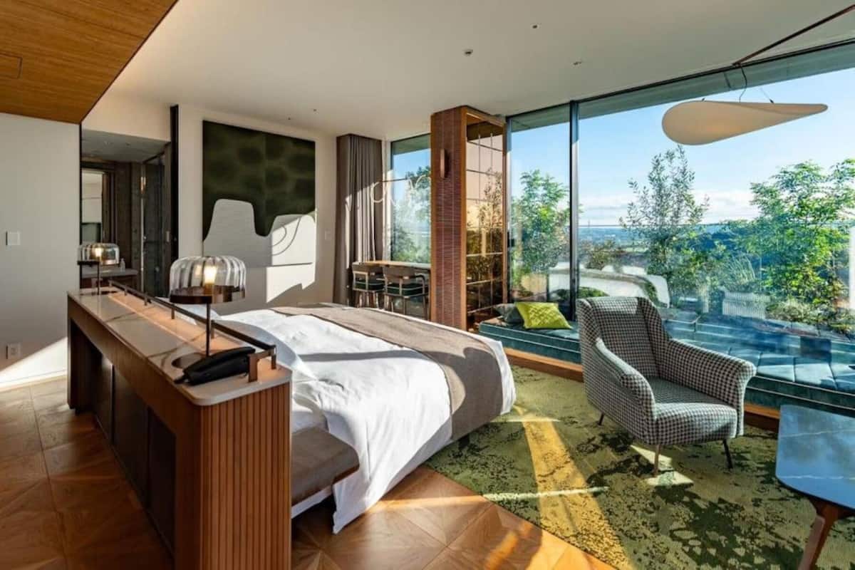 A modern bedroom with a large bed, a desk, a chair, and a view of the outdoors.