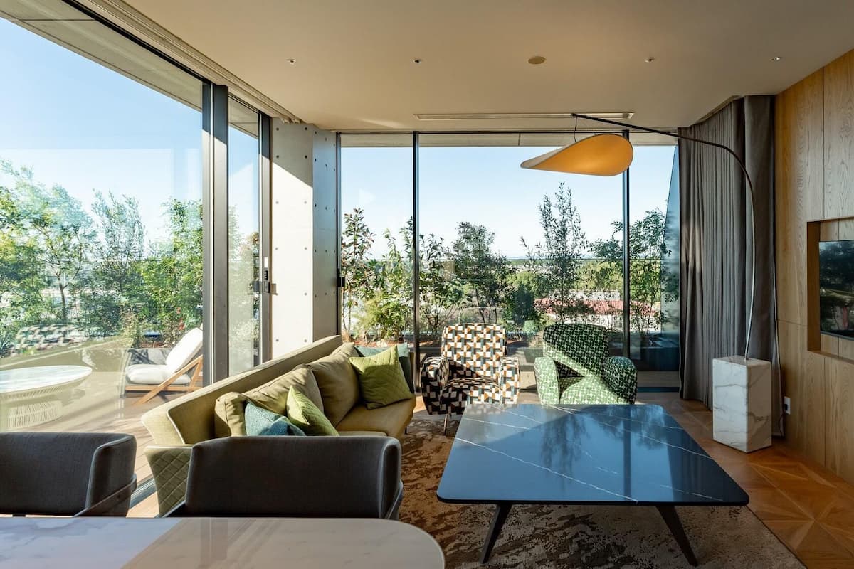 A modern living room with a glass wall, a sofa, a coffee table, and a TV mounted on the wall.
