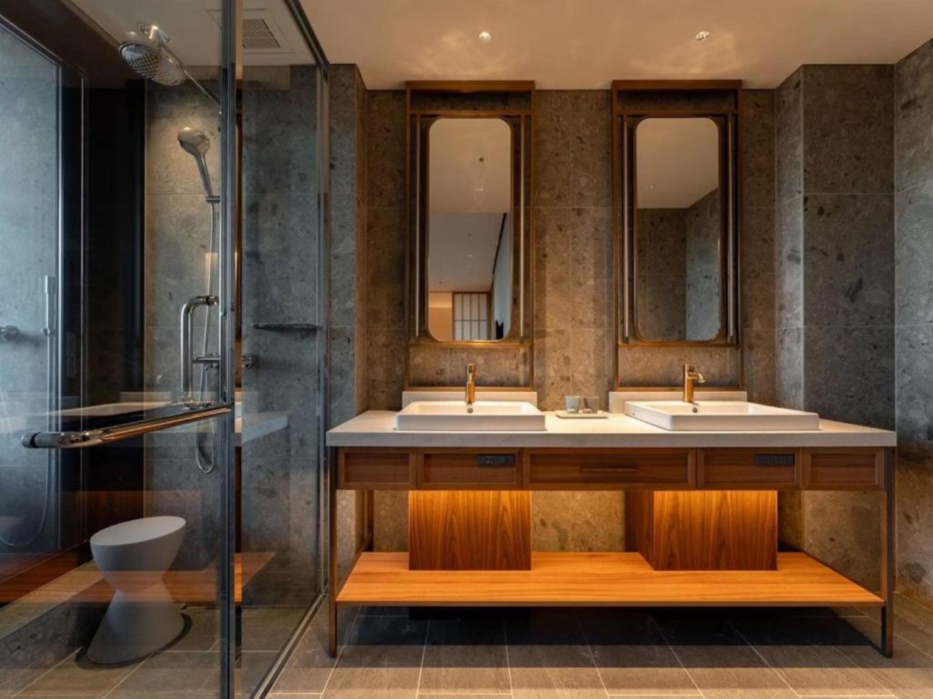 A modern bathroom with a glass shower enclosure, two sinks, and a wooden vanity.