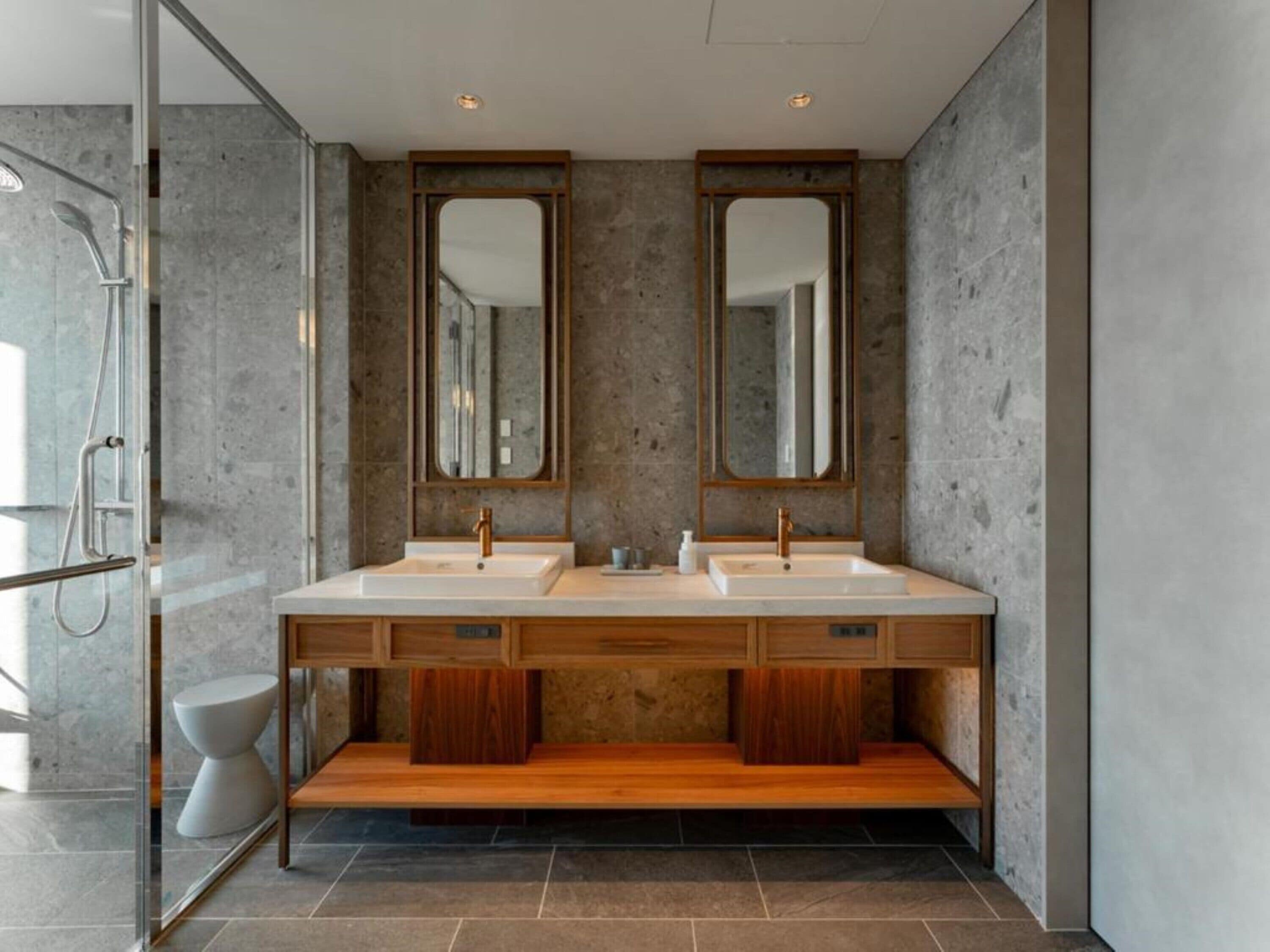 Un baño moderno con dos lavamanos, tocador de madera y espejos grandes.