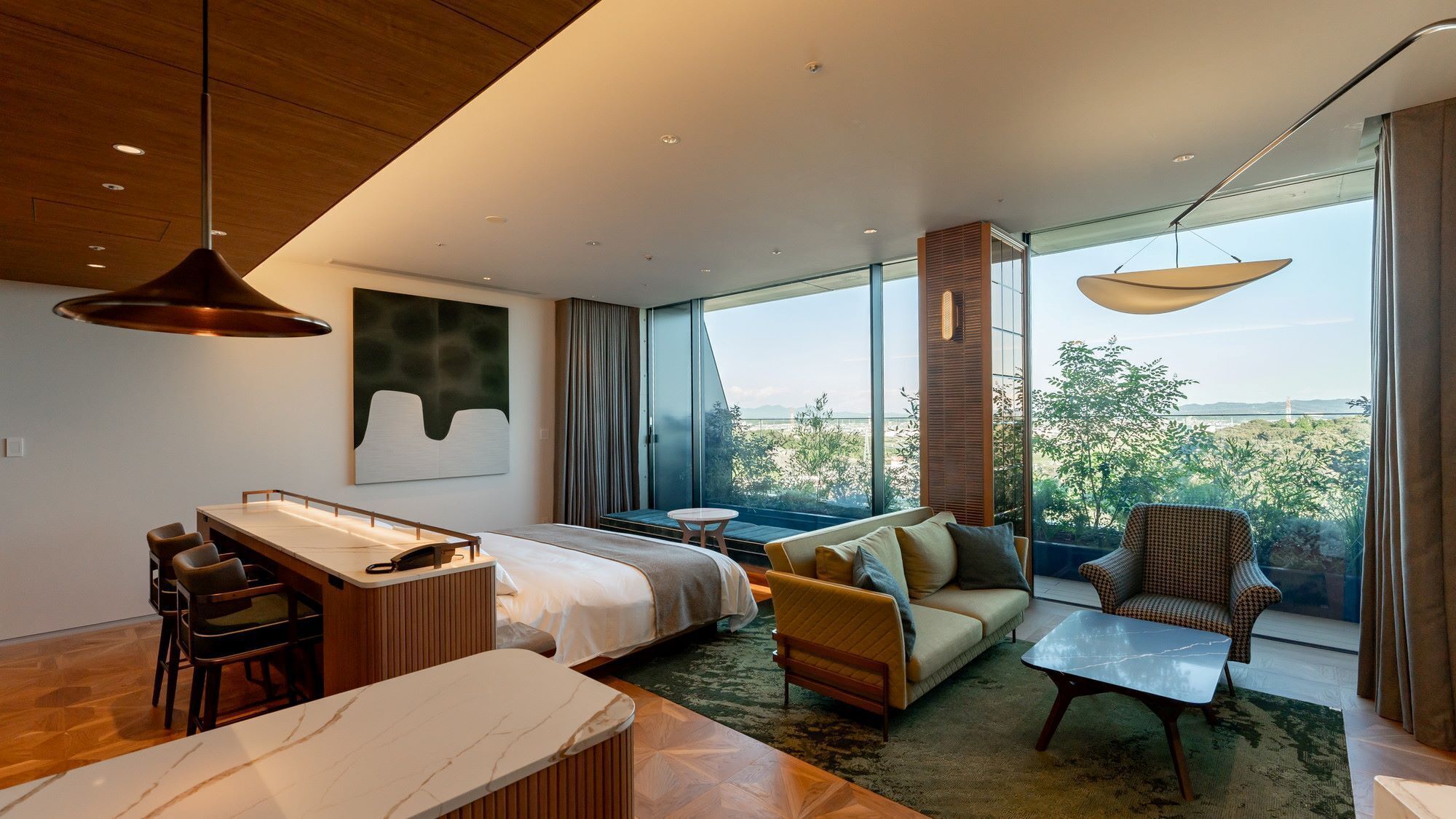 Een moderne hotelkamer met een bed, een bank, fauteuil en een zithoek met tafel en stoelen.