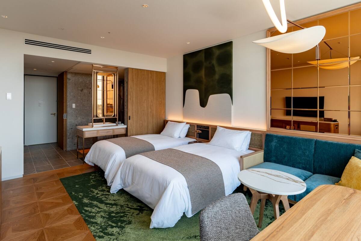 A hotel room with two beds, a sofa, a small table, and a TV.