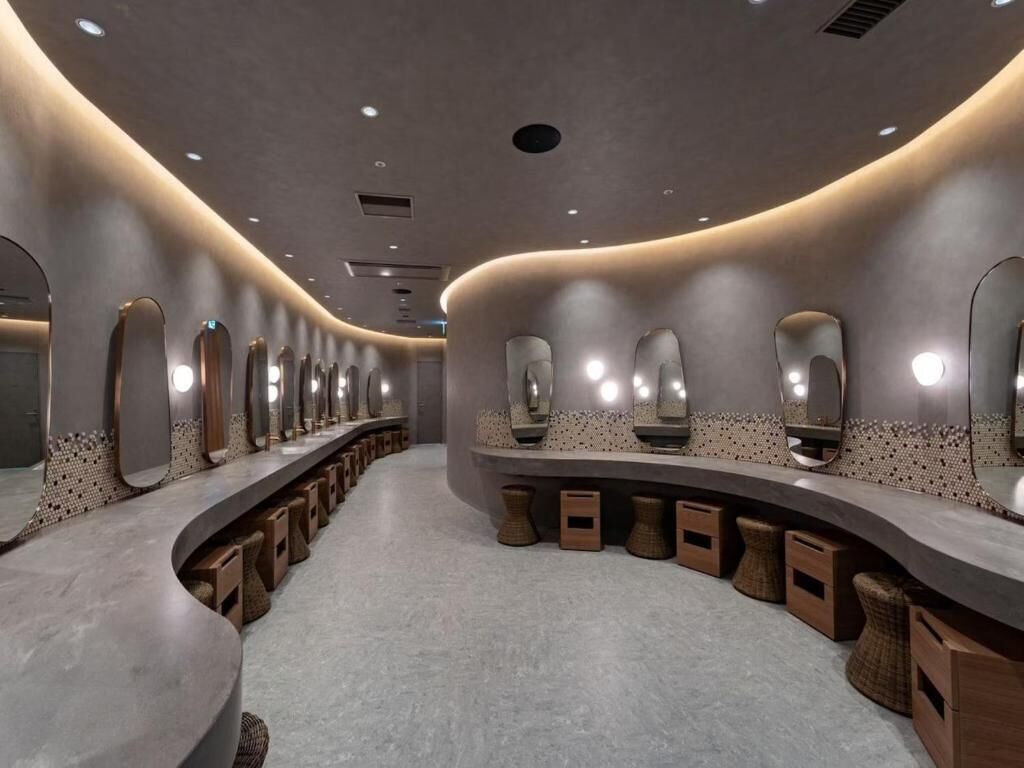 Un baño moderno con diseño curvo, varios espejos y taburetes de madera.