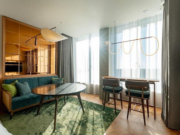 A modern living room with a sofa, a dining table with chairs, a large window with curtains, and a hanging light fixture. - GREENITY IWATA (Iwata)