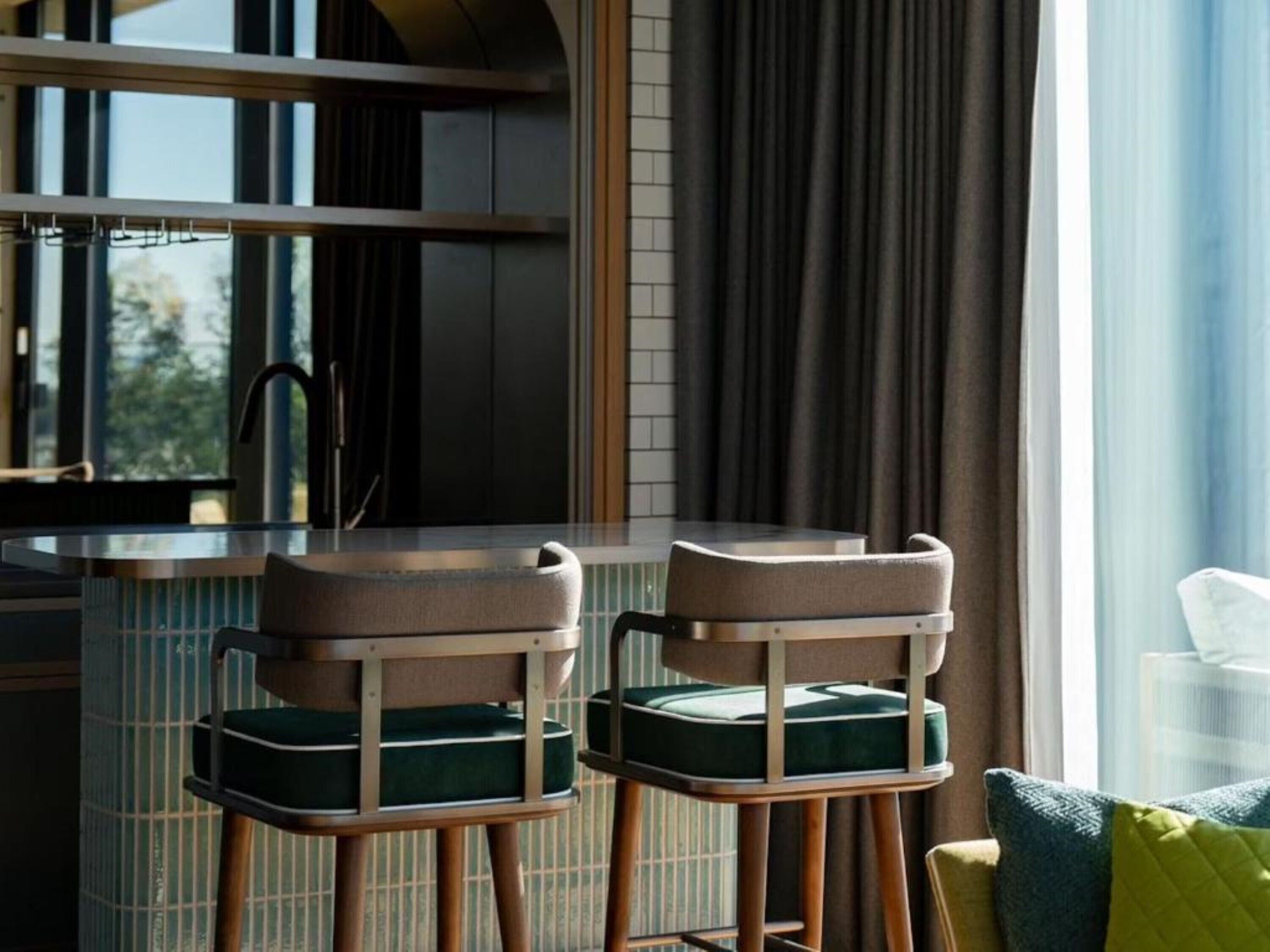 A modern kitchen with a bar area, featuring two bar stools with cushioned seats and wooden legs.