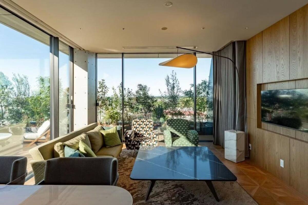 A modern living room with a glass wall, a sofa, a coffee table, and a TV mounted on the wall.