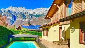 A pool area with a mountain backdrop, a wooden deck, and a building with solar panels. - Cozy Accomodation Retreat (Quarten)