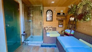 A wooden interior with a glass shower, a bed with a blue mattress, and a wicker sofa. - Cozy Accomodation Retreat (Quarten)