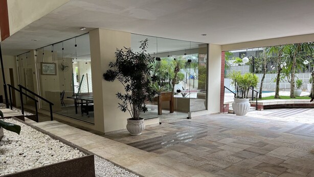En rymlig entréhall med en vägg av glas, en stor krukväxt och ett klinkergolv.