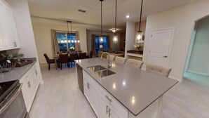 A modern kitchen with a central island, white cabinetry, and pendant lighting. - Luxury 6B Pool Home At Storey Lake (Kissimmee)