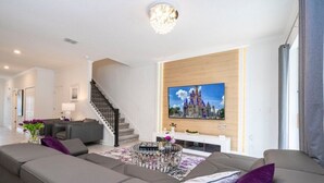 Una sala de estar moderna con un televisor de pantalla plana grande montado en una pared de madera, un sofá gris, una mesa de centro con objetos decorativos y una escalera que conduce a otro nivel.