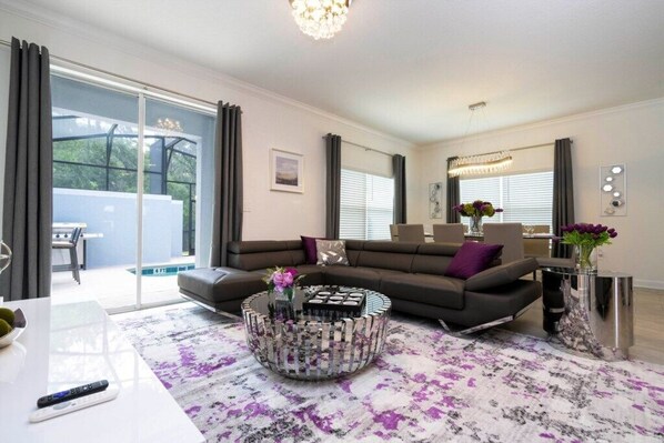 A modern living room with a sectional sofa, a coffee table, and a glass-top dining table. - Wonderful 5 Bedrooms Homes - Near Disney (Kissimmee)