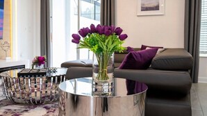 Una sala de estar moderna con una mesa de centro de vidrio, un sofá y un jarrón con flores moradas.