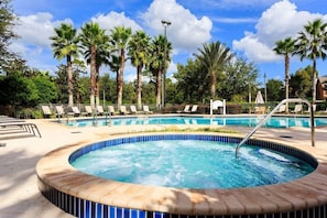 Un área de piscina con sillones de descanso y palmeras.