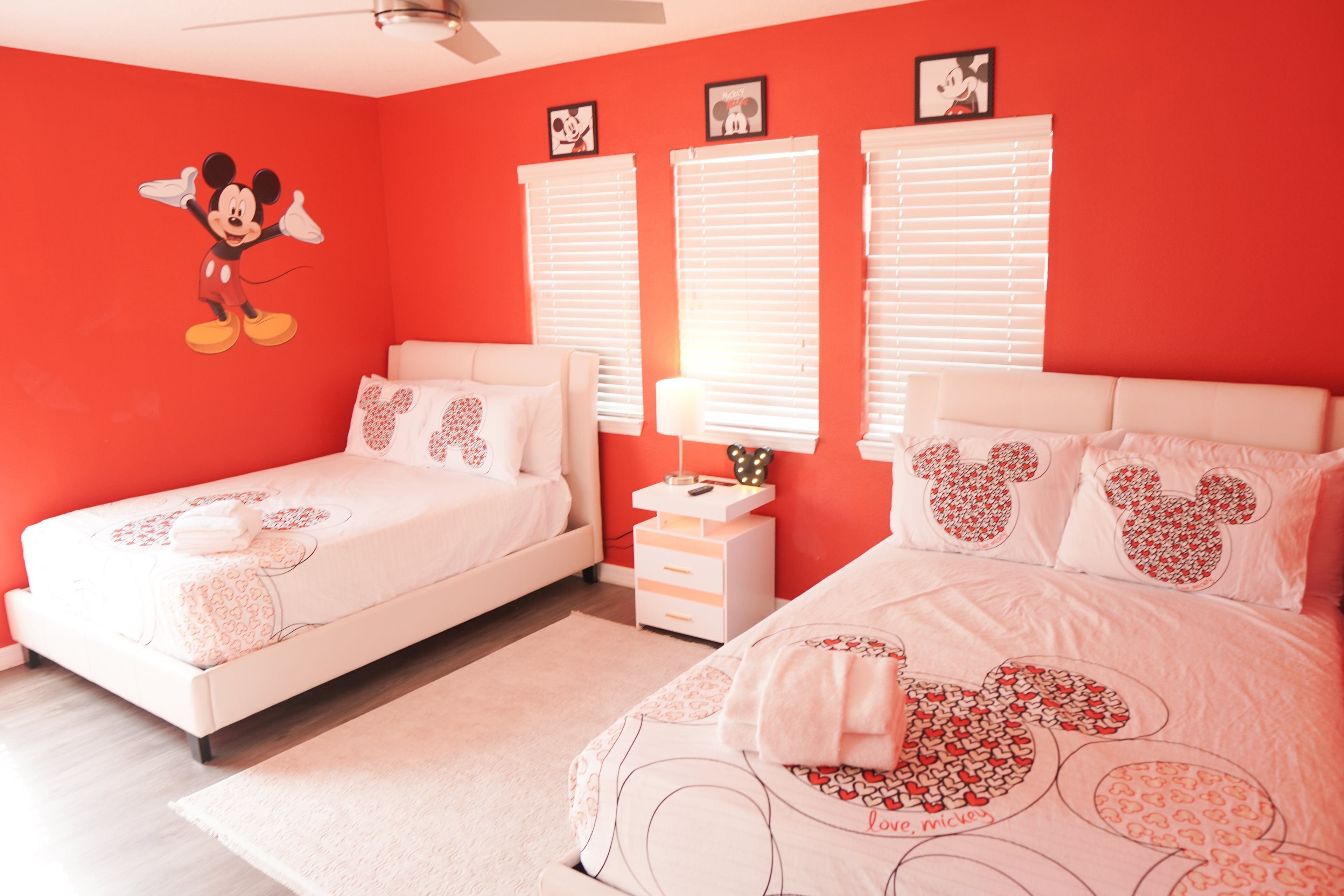 Un dormitorio con dos camas, paredes rojas y decoración temática de Mickey Mouse.