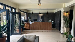 Uma área de recepção com balcão de madeira, estátua de Buda e plantas em vasos.