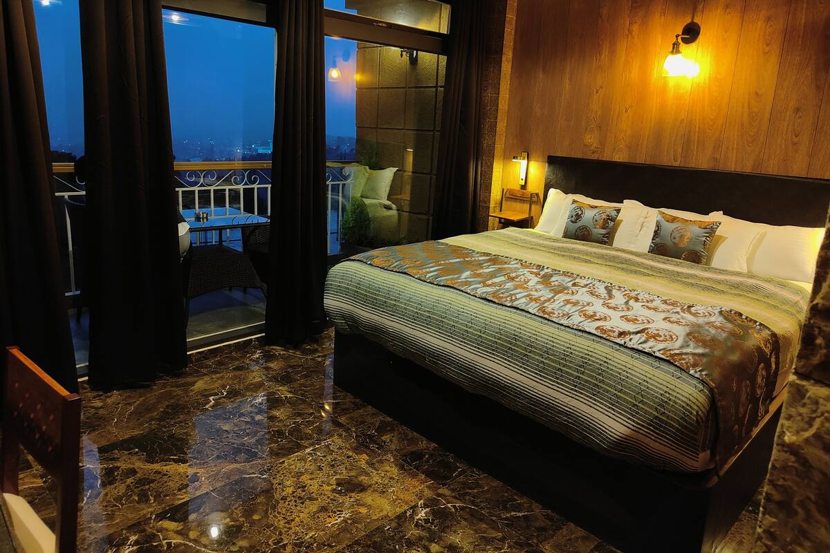 A hotel room with a large bed, a balcony with a view, and a wooden wall.