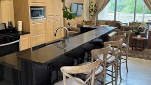 Una cocina moderna con una isla central, armarios de madera y un comedor con sillas de mimbre.