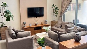 Una sala de estar moderna con una televisión de pantalla plana, sofás, una mesa de centro y plantas en macetas.