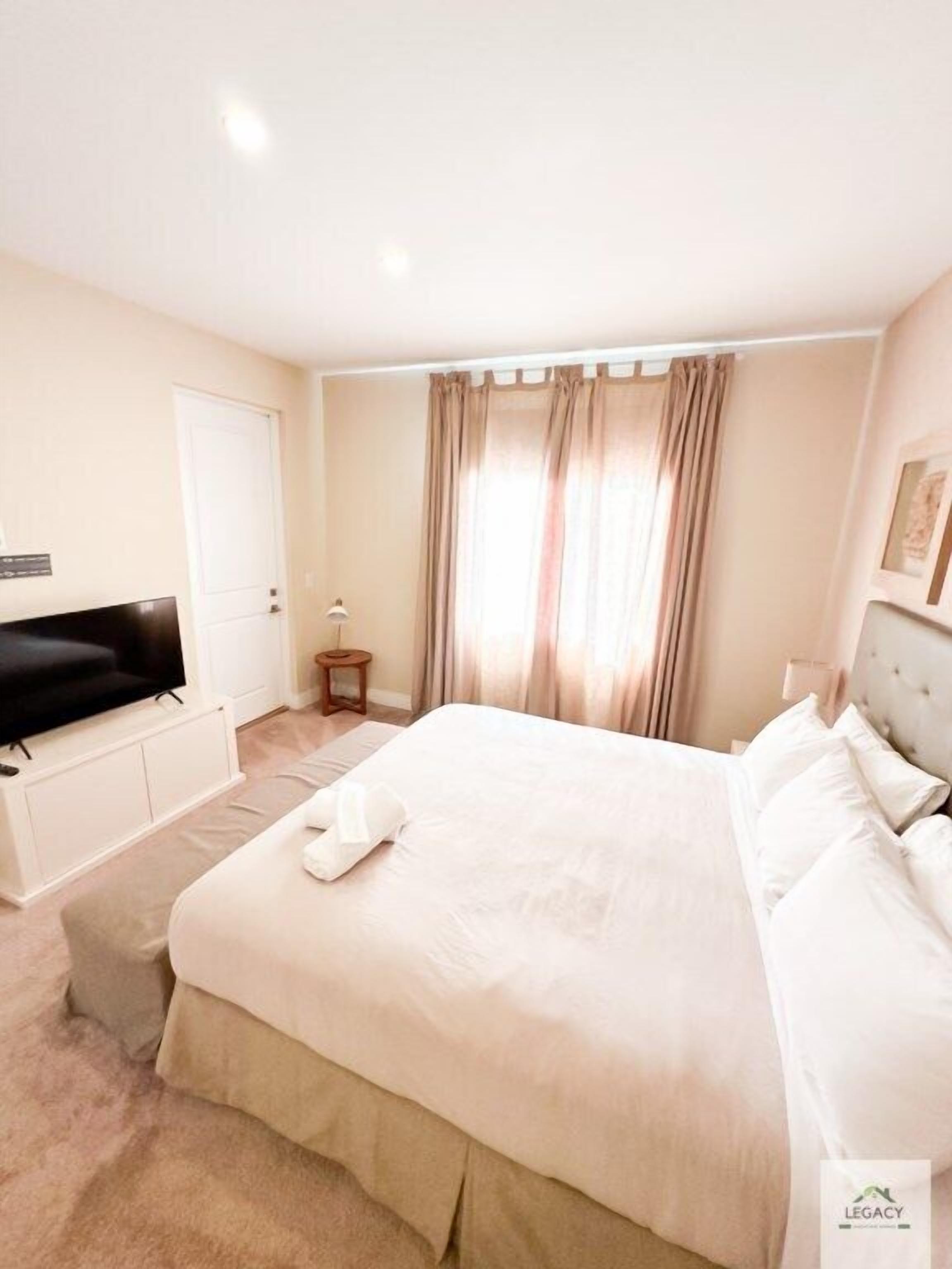 Quarto de hotel com uma cama grande, televisão, mesa de cabeceira pequena e janela com cortinas.