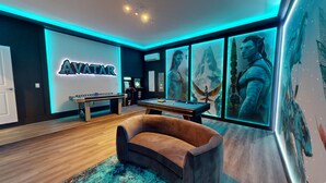 Une pièce équipée d’une table de billard, d’un canapé et d’un mur orné d’une enseigne lumineuse représentant le mot « AVATAR ».