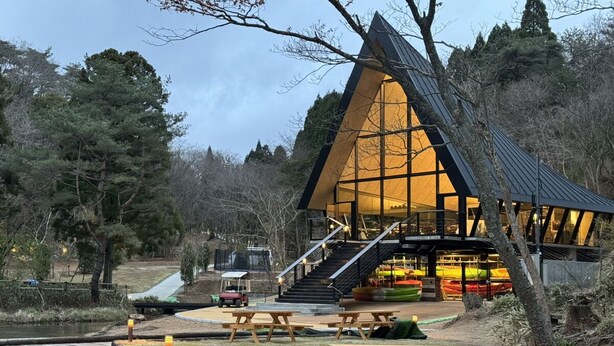 A modern building with a triangular roof, wooden picnic tables, and a dock extending into a body of water. - kobe city shizennoie - Hostel (Kobe)
