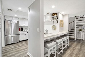 A modern kitchen with stainless steel appliances, a white countertop, and a built-in bar with stools.