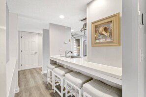 A modern kitchen with a white countertop, a sink, and bar stools. - Walk to Beach & Golf | 2 BR Palmetto Dunes Villa (Hilton Head Island)