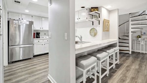 Una cocina moderna con armarios blancos, electrodomésticos de acero inoxidable y una zona de bar con taburetes.