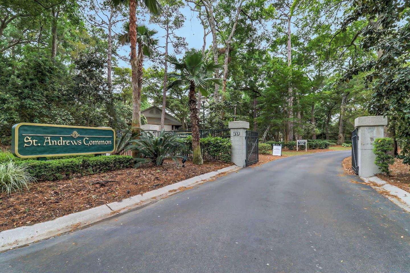 A gated entrance to St. Andrews Commons with a sign, a paved driveway, and surrounding greenery.