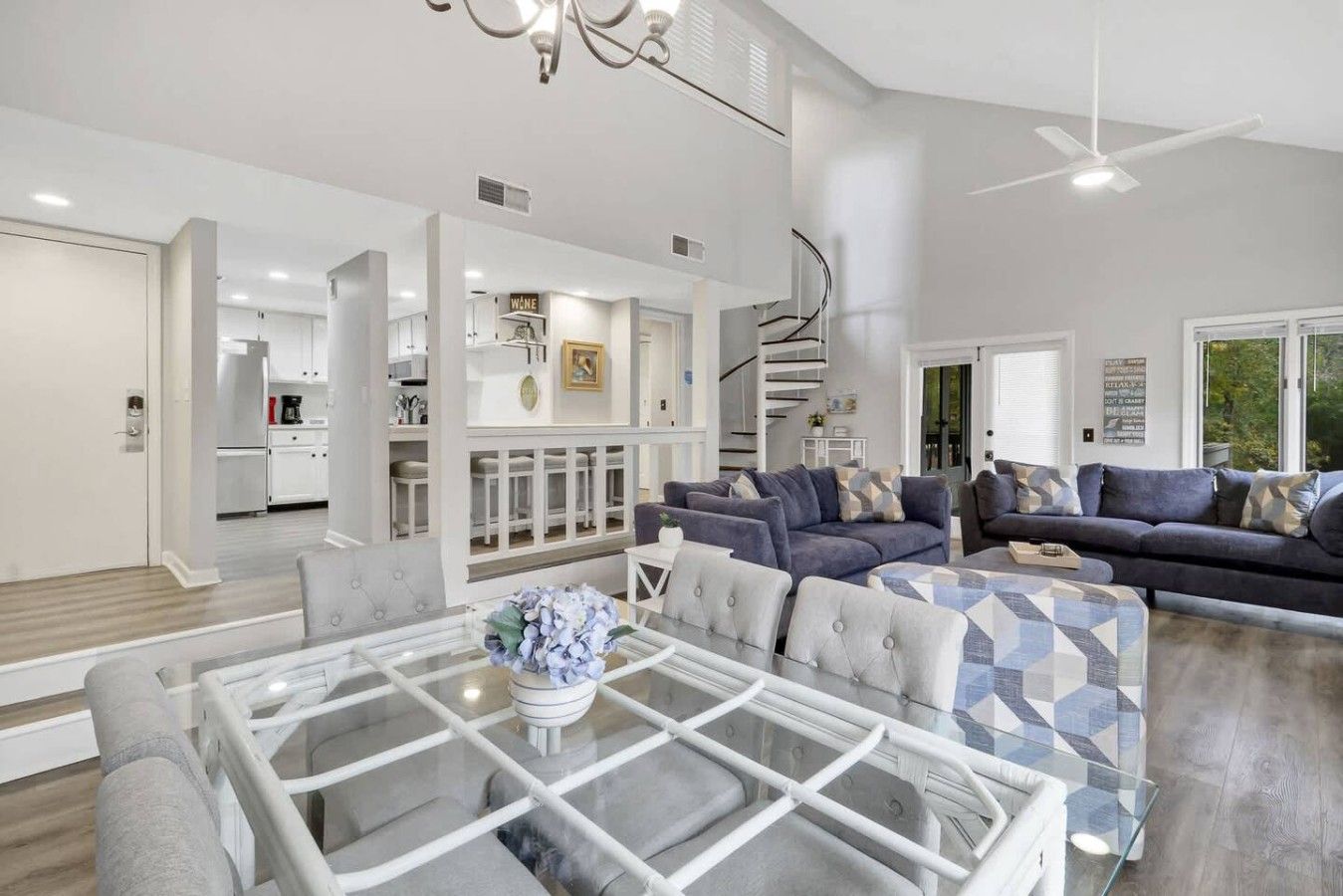 A spacious living area with a glass coffee table, a sofa set, and a kitchen in the background.