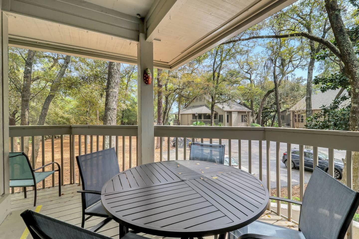 A covered outdoor seating area with a table and chairs, overlooking a residential street and trees.