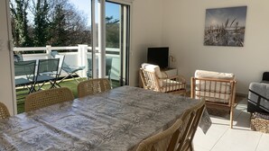 A dining area with a table and chairs, a television on a stand, and a view of the outdoors through large sliding doors.