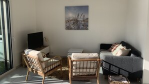 A modern living room with a sofa, two wicker chairs, a flat-screen TV, and a painting on the wall.