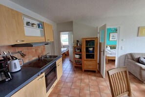A compact kitchen with modern appliances, wooden cabinets, and a dining area with a sofa.