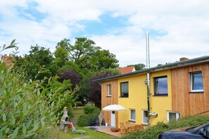 A yellow building with a wooden facade, a satellite dish, and a patio with outdoor furniture.